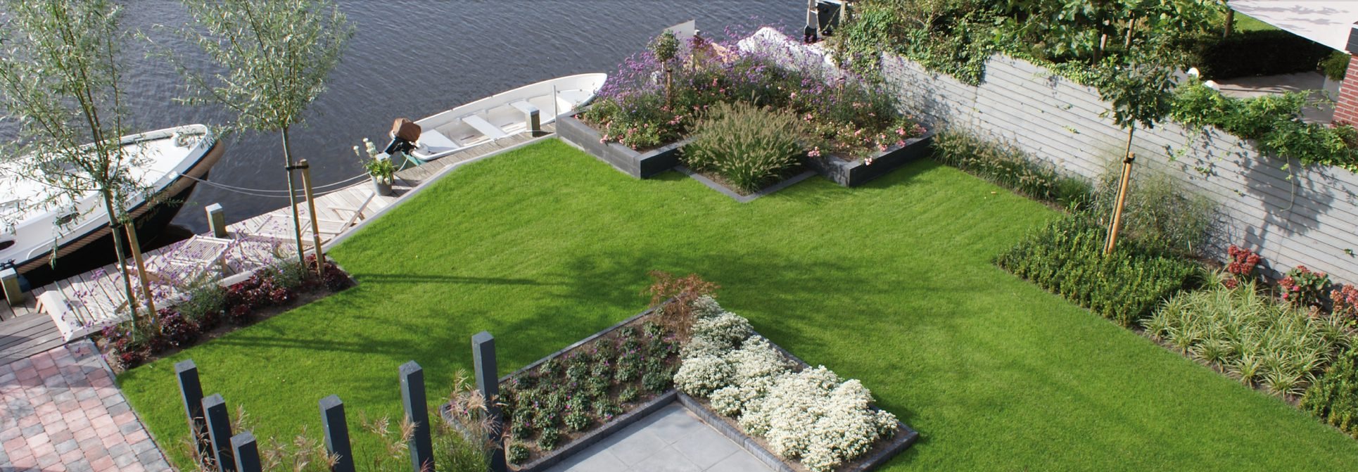 Tuin met gazon, borders en terras aan het water